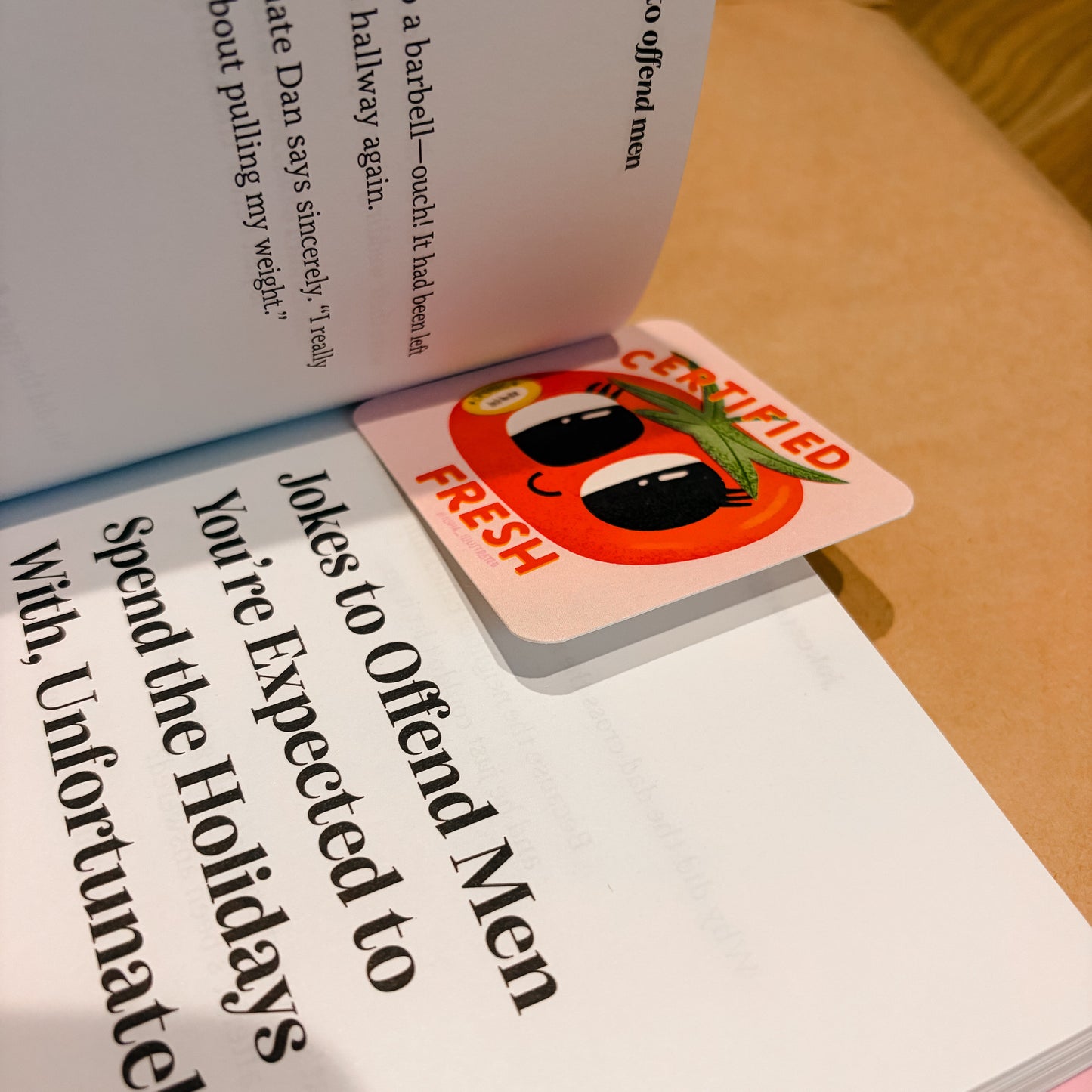 A square pink bookmark or card with a cartoon tomato face and the words 'CENSORED FRESH' resting on open book pages.
