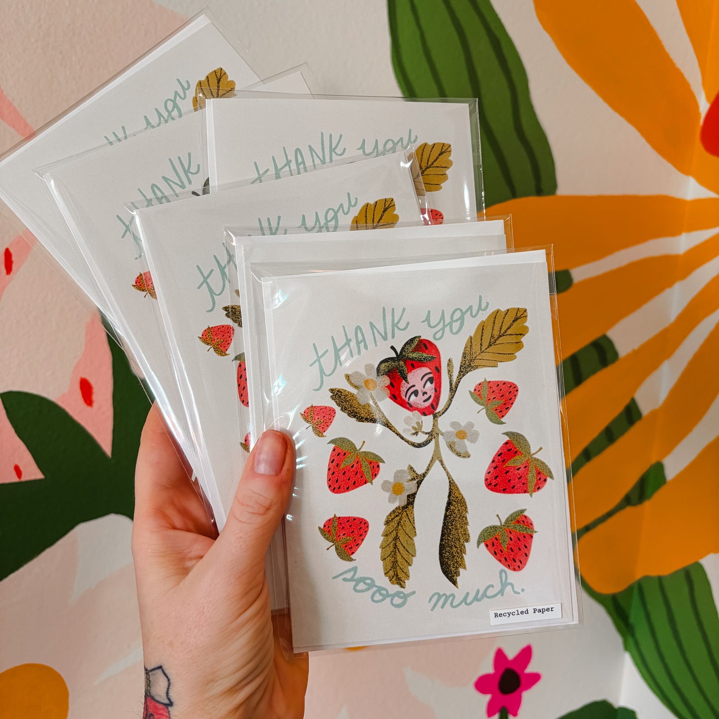 Hand holding a set of greeting cards with strawberry design on a colorful floral background