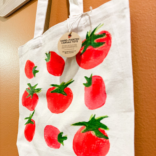 White tote bag with red tomato designs on a brown surface