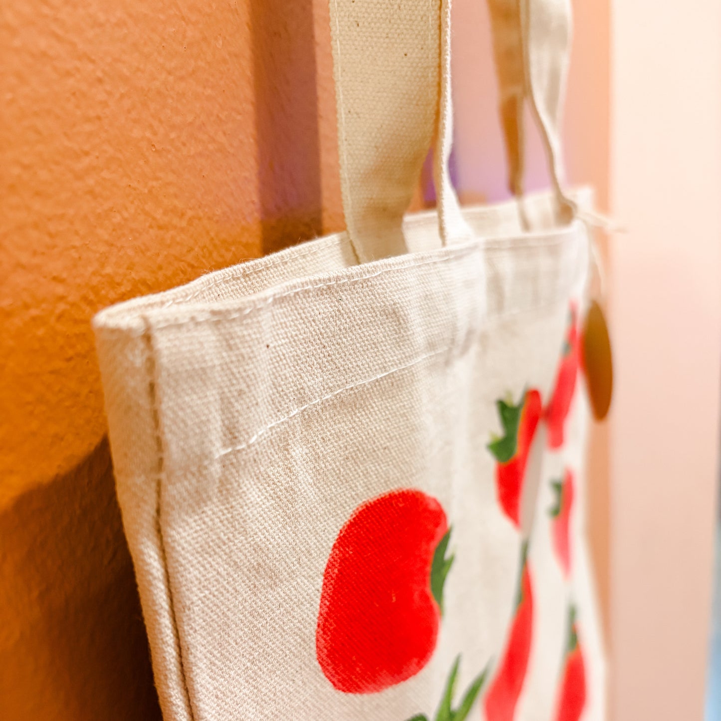 Beige tote bag with red tomato design on a peach-colored wall.