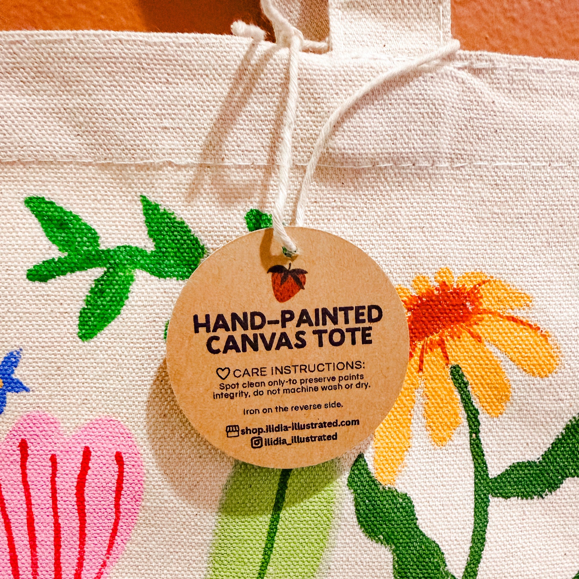 Hand-painted canvas tote bag with floral designs and a care label.