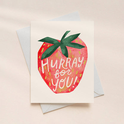 Greeting card with strawberry design and 'Hurray for you!' text on a beige background