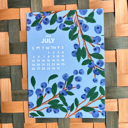 July 2026 calendar card with blueberry design on a woven surface