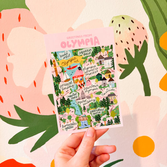 Hand holding a colorful Olympia map postcard 4x6 with 'Olympia' branding against a vibrant, abstract background.