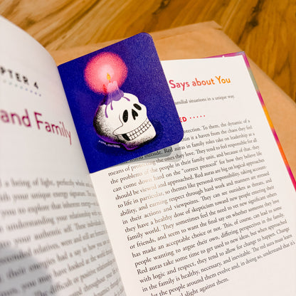 An open book spread photographed from above on a wooden surface, showing printed text on both pages with a colorful illustration on the left page featuring a skull and a pink glowing orb.
