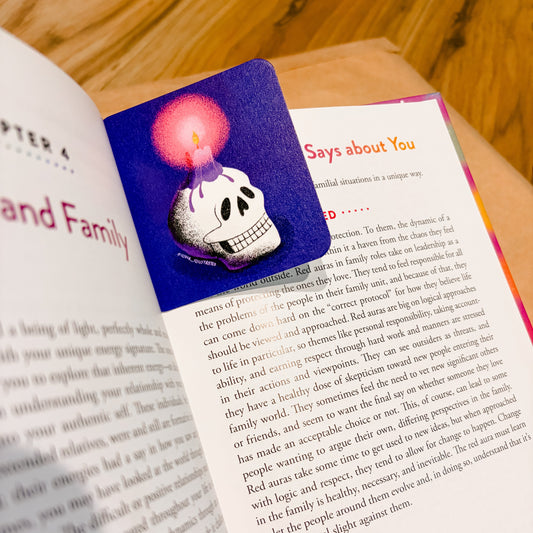 An open book spread photographed from above on a wooden surface, showing printed text on both pages with a colorful illustration on the left page featuring a skull and a pink glowing orb.