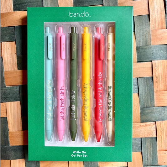 Set of six colorful gel pens in a green Bando packaging on a woven wooden surface.