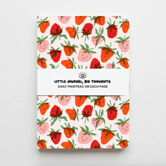 A notebook with a white cover featuring a repeating pattern of cute, smiling strawberries in red, pink, and orange with green leaves. A white paper band wrapped around the center reads 'LITTLE JOURNAL, BIG THOUGHTS' and 'DAILY MANTRAS ON EACH PAGE'.