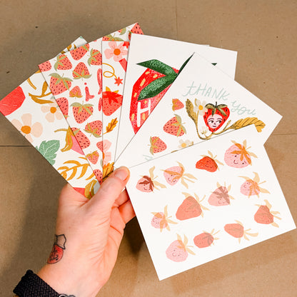 Hand holding a set of strawberry-themed cards against a brown background