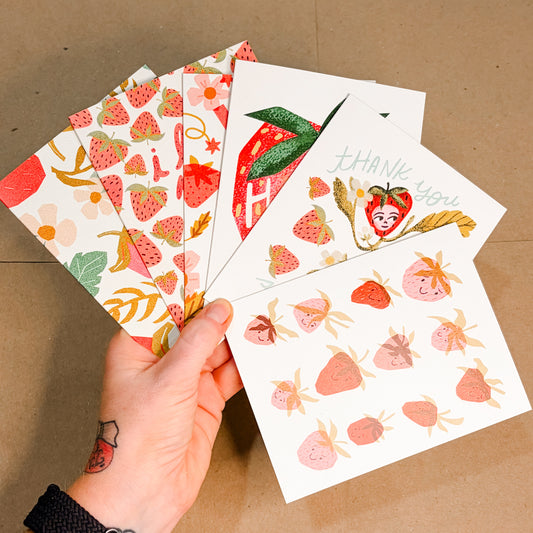 Hand holding a set of strawberry-themed cards against a brown background