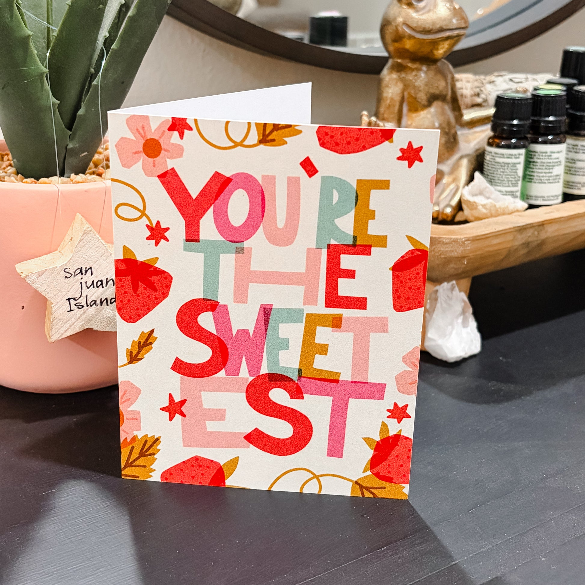 Card with 'You're the Sweetest' text on a surface with decorative items in the background