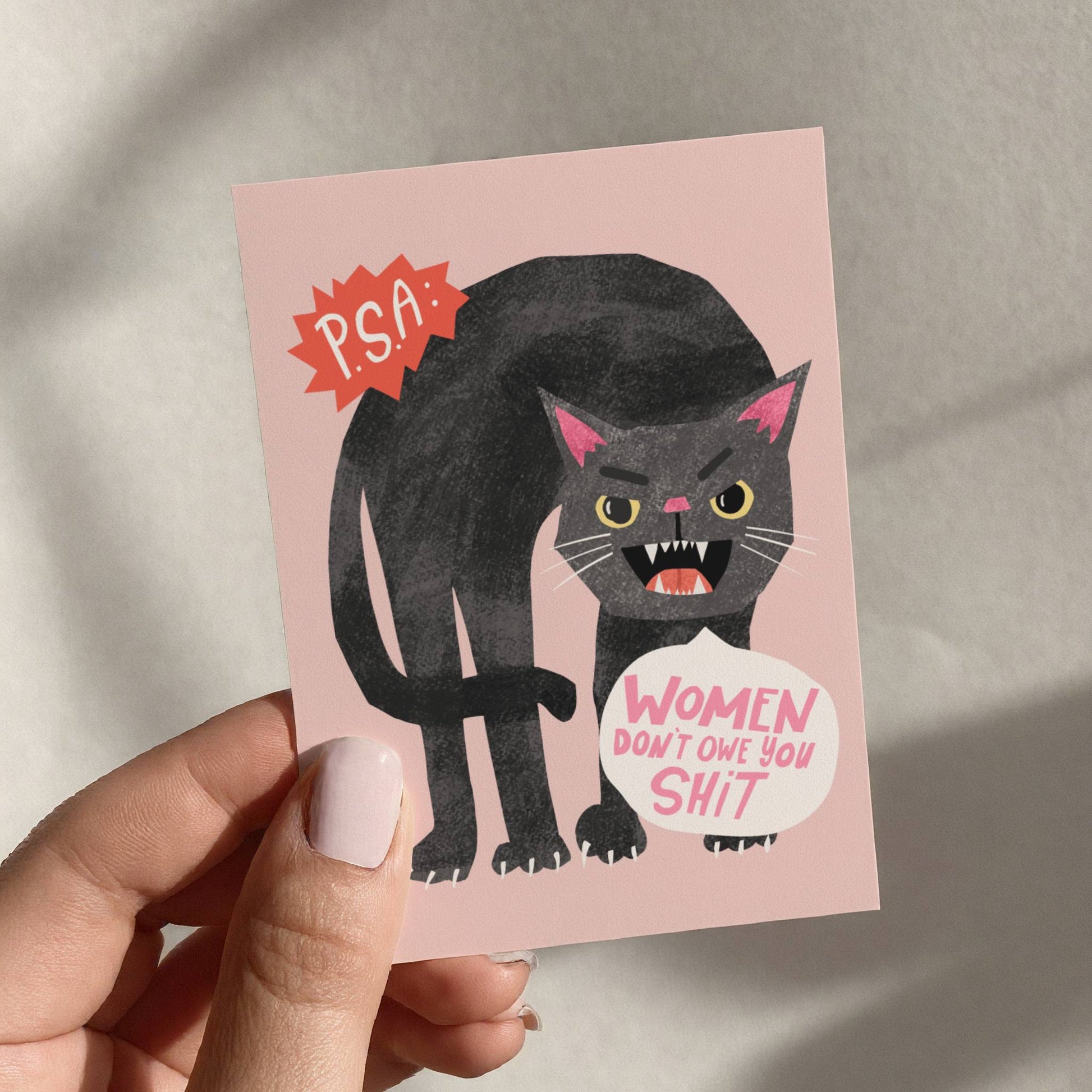 Card with a black cat illustration and text held by a hand against a neutral background
