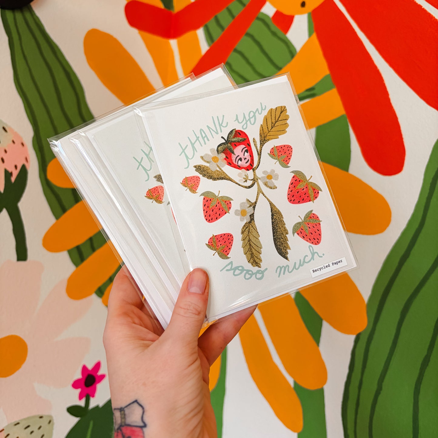 Hand holding a card with strawberry design against a colorful floral background
