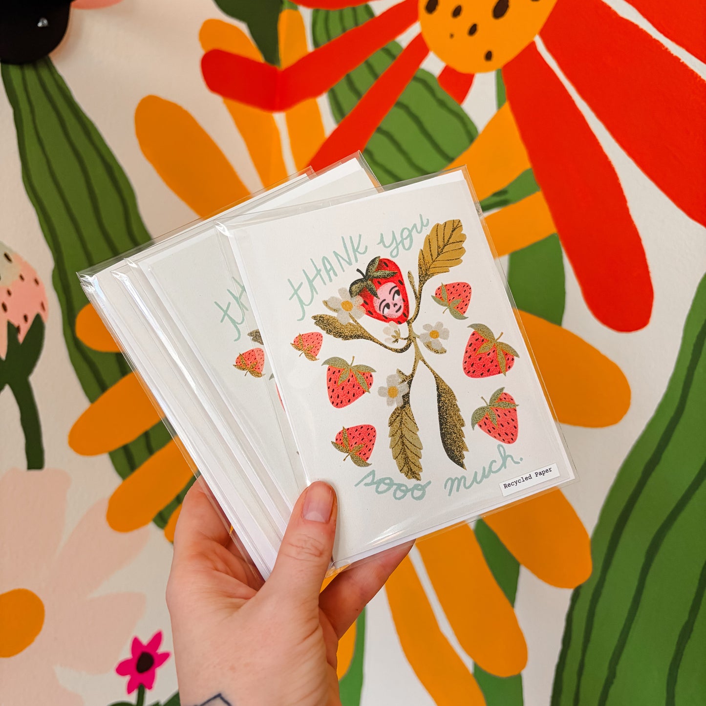 Hand holding a card with strawberry design against a colorful floral background