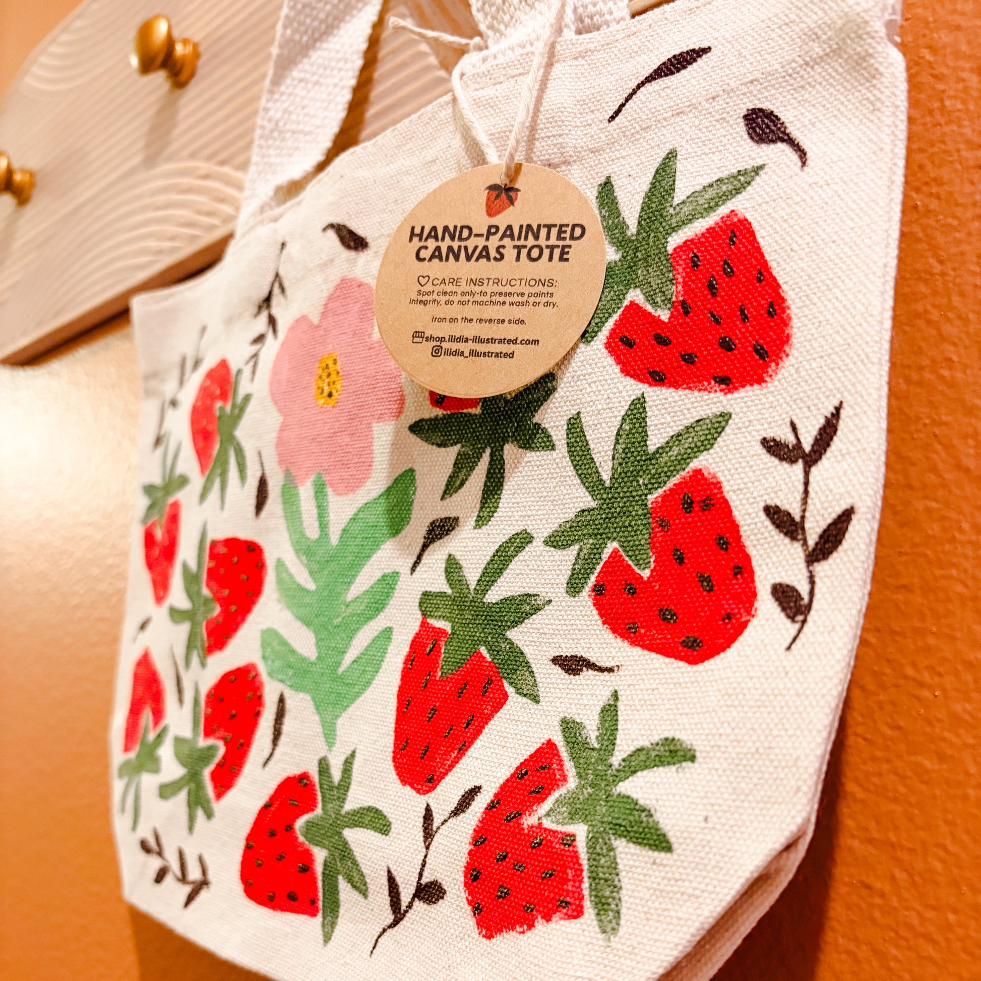 Hand-painted canvas tote bag with strawberry design on an orange background