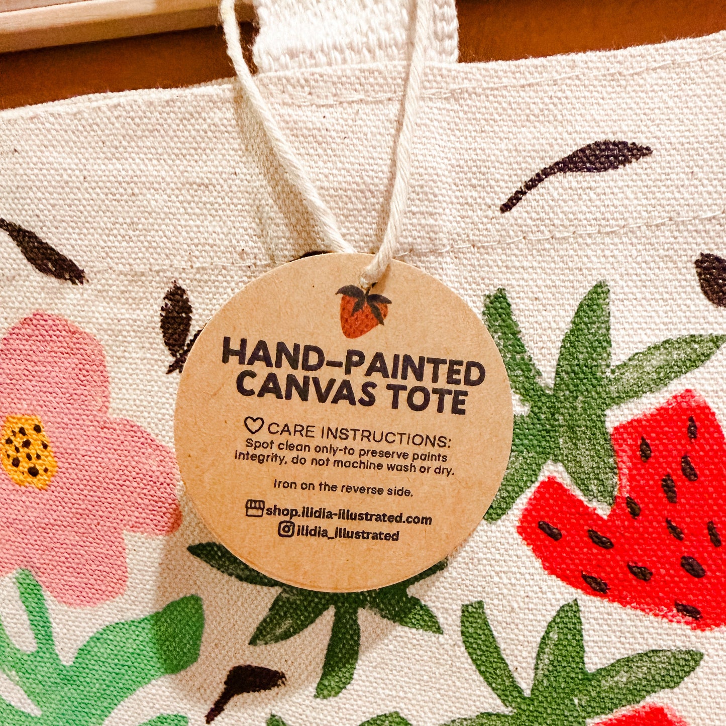 Hand-painted canvas tote bag with strawberry and flower design and care tag.
