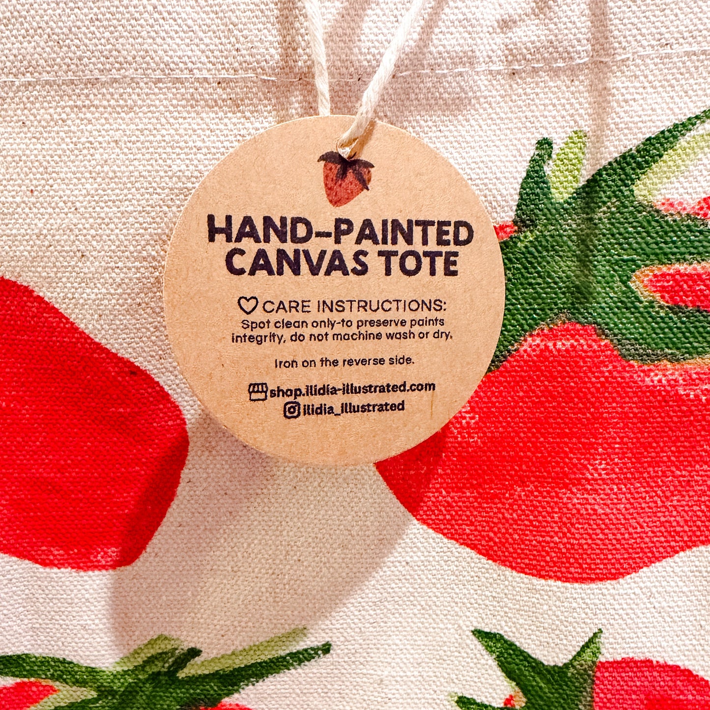 Hand-painted canvas tote with tomato design and care tag.